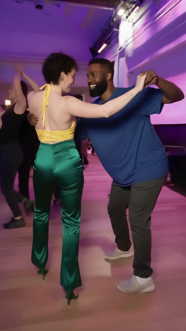 A man in a blue t-shirt and a woman in green satin pants smiling joyfully while dancing bachata